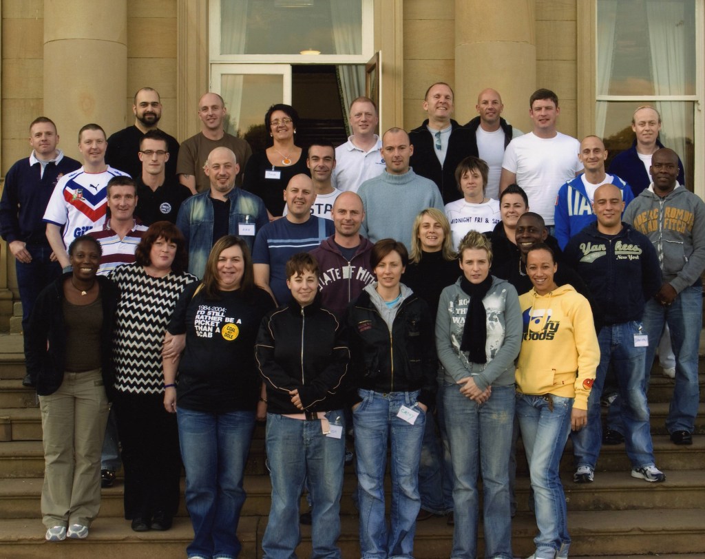 A group of people standing together and smiling on the steps of a large stone building with its glass doors open.