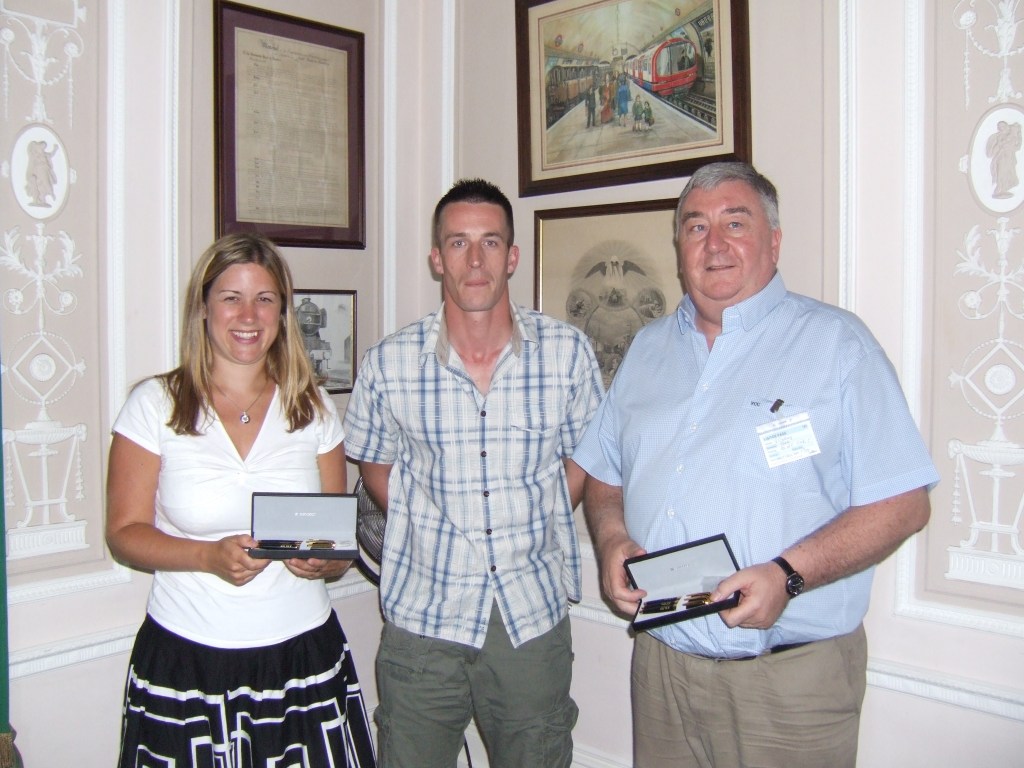 Ellie Reeves and Vic Codling are holding presentation boxed pens and standing either side of an ASLEF member in front of vintage rail photographs. 